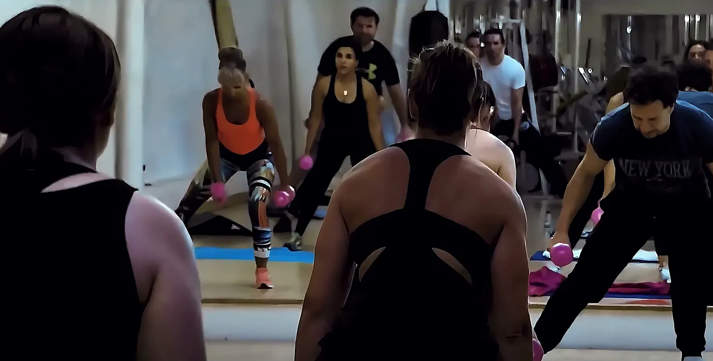 Groupe d’adhérents en fentes avec haltères, guidés par le coach face au miroir