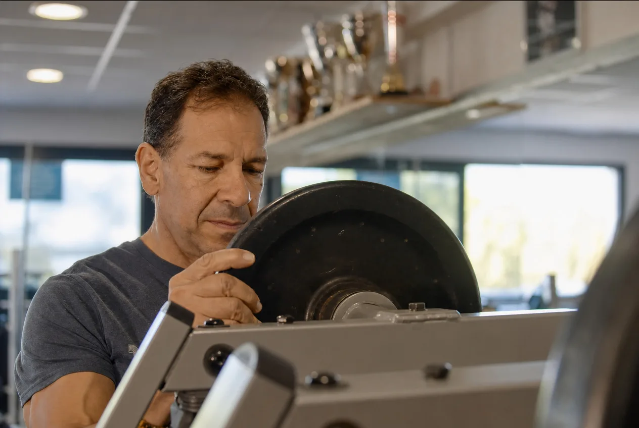 Adhérent d’ABS Sport Gym chargeant un disque sur une machine, trophées du club en arrière-plan